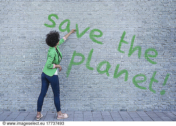 Young woman writing Save the Planet on wall