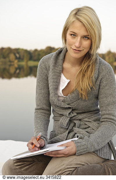 Young woman writing sketching  by lake
