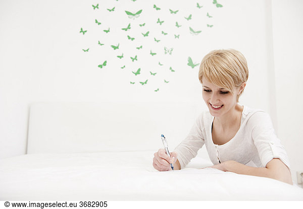 Young woman writing sketching on bed