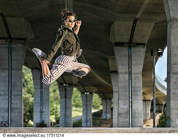 Young womann doing acrobatics and jumping under bridge
