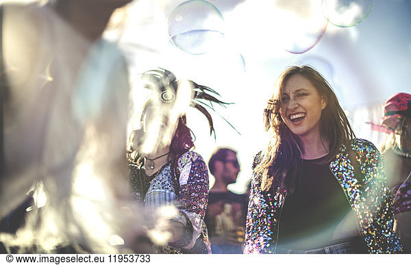 Young women at a summer music festival wearing sequined jacket  dancing.