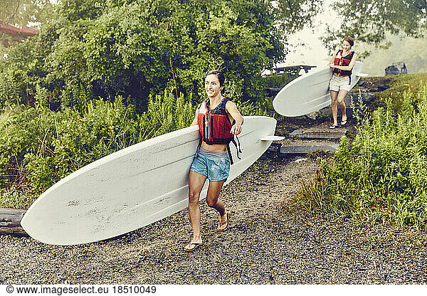 Young women carry their paddle boards down to the water on a foggy day