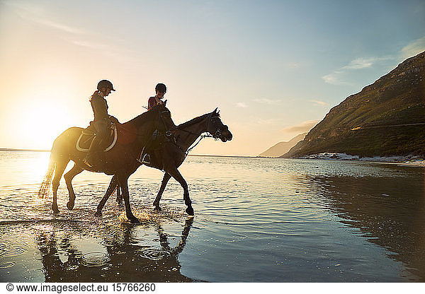 Young women horseback riding in sunny sunset ocean surf