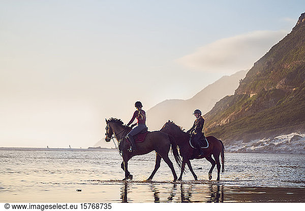 Young women horseback riding on tranquil ocean beach