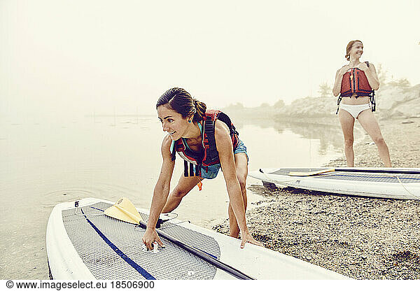 Young women launch their paddle boards into water on a foggy morning