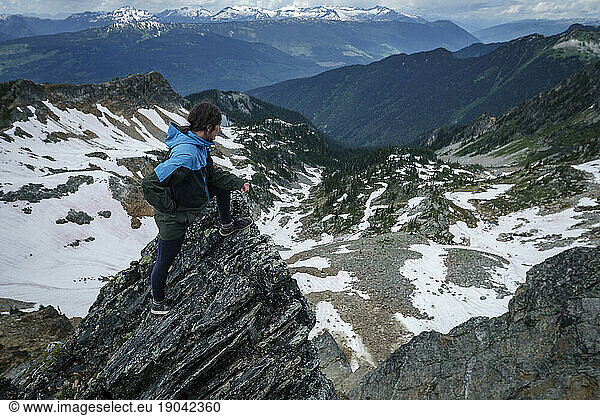 Young women on rock looks down to valley of mountains and snow  Canada