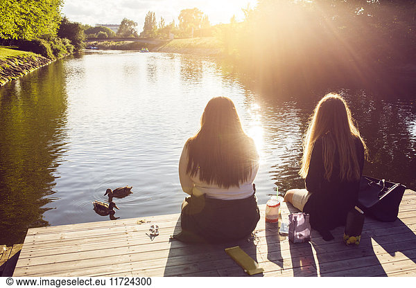 Young women sitting on pier and looking at ducks