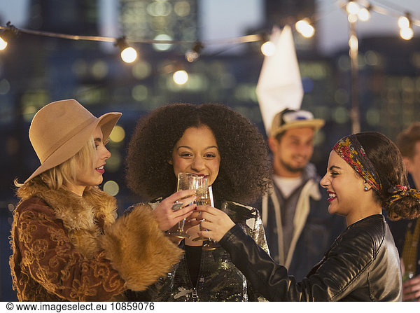 Young women toasting champagne glasses at nighttime rooftop party