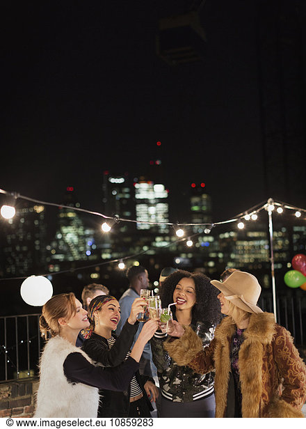 Young women toasting cocktails at nighttime rooftop party