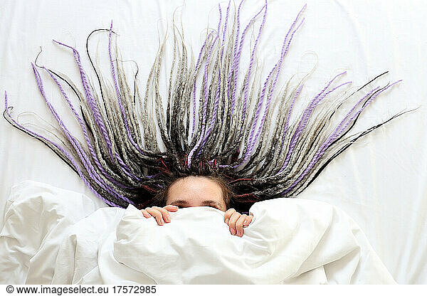 Young women with dreadlocks is hiding under the blanket