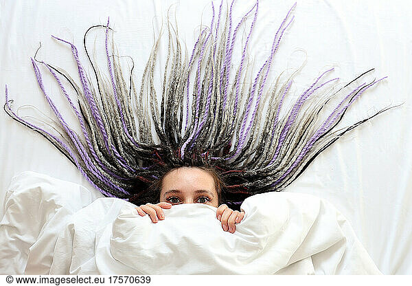 Young women with dreadlocks is peeping out under the blanket
