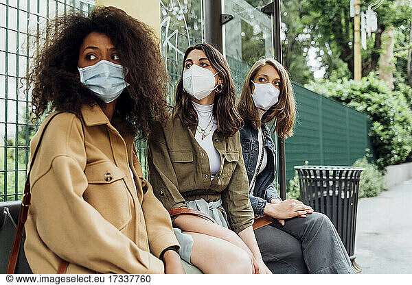 Young women with protective face mask sitting at bus stop