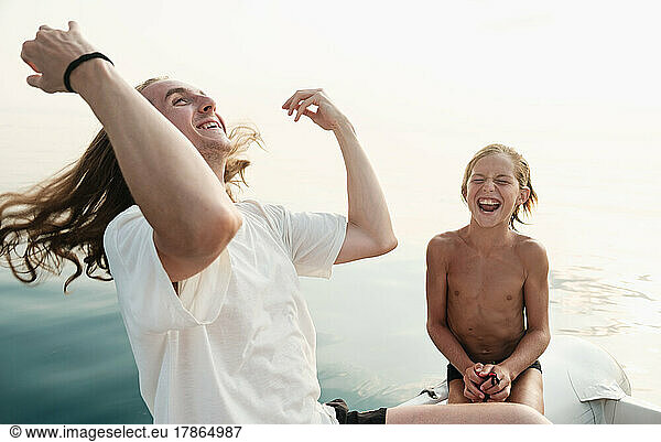 Younger and older brothers having fun and laughing in the boat in sea.