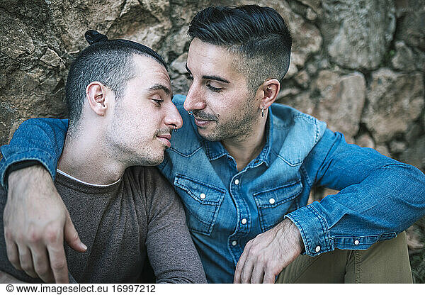 Zärtliche homosexuelle Männer sitzen an einer Steinmauer