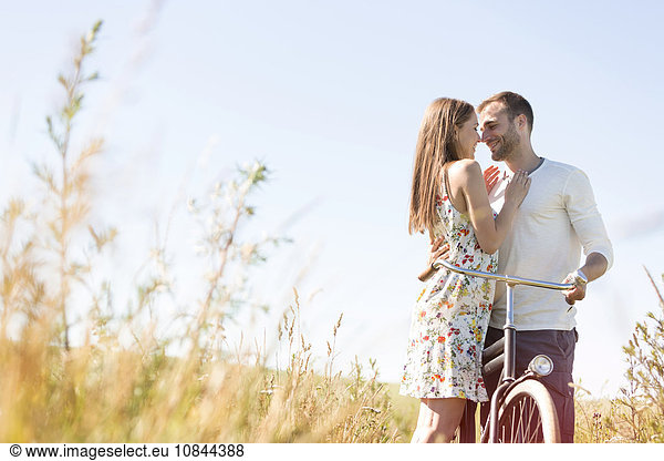 Zärtliches junges Paar mit Fahrradumarmung im sonnigen ländlichen Gebiet