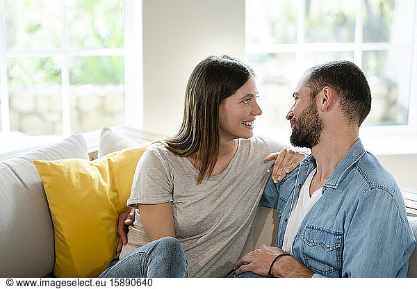 Zärtliches junges verliebtes Paar  das sich zu Hause auf der Couch anlächelt