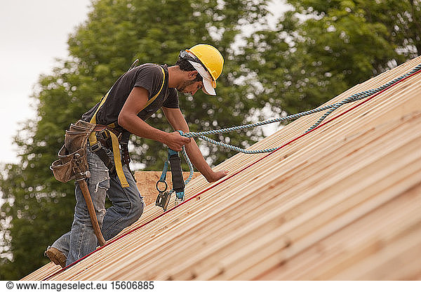 Zimmermann mit Sicherheitsgurt auf dem Dach eines im Bau befindlichen Hauses