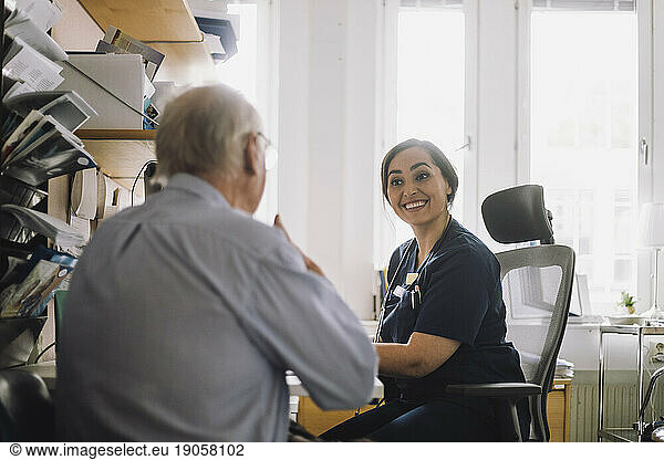 Zufriedene Krankenschwester  die einem älteren männlichen Patienten bei einem Besuch in der Klinik zuhört