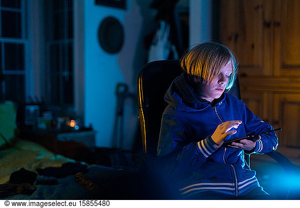 Zuhause sitzender Junge sitzt zu Hause und arbeitet am Tablett  während er auf einem Stuhl sitzt