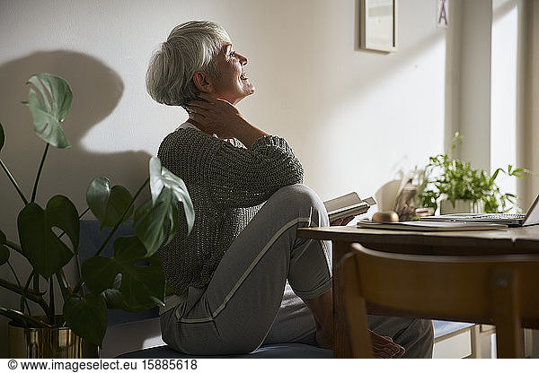 Zuversichtliche ältere Frau mit Notebook und Laptop entspannt zu Hause