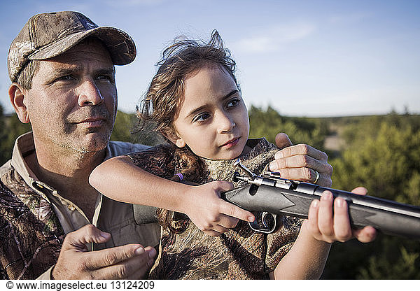 Zuversichtliches Mädchen zielt Gewehr mit Vater auf dem Feld