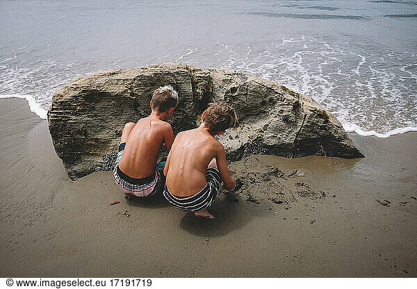 Zwei Brüder in Badehosen graben Sand am Strand