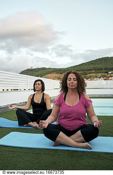 Zwei Frauen üben Yoga auf der Terrasse des Hauses  Lotussitz