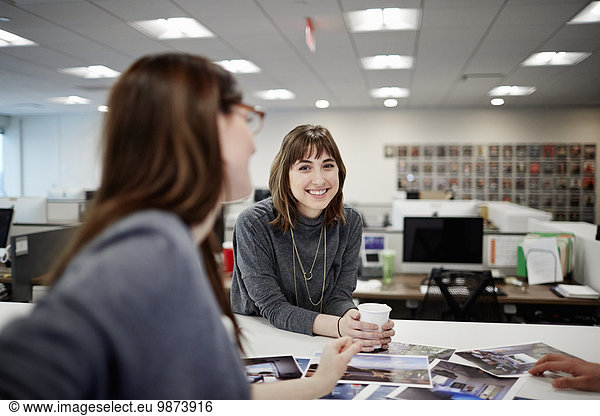 Zwei Frauen sitzen in einem Büro und unterhalten sich unterhaltend und lachend.