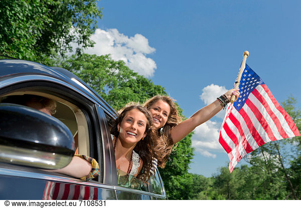 Zwei Freunde  die sich aus dem Autofenster lehnen und die amerikanische Flagge halten.