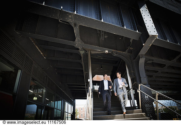 Zwei Geschäftsleute in grauen Anzügen gehen am Eingang eines Gebäudes eine Treppe hinunter.