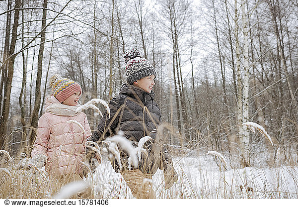 Zwei Geschwister gehen Hand in Hand im Winterwald