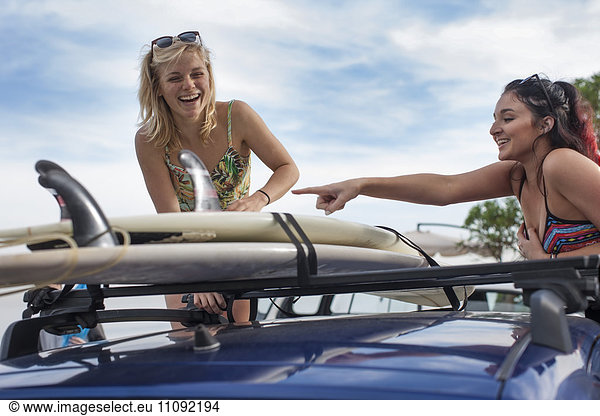 Zwei glückliche junge Frauen beim Auspacken von Surfbrettern im Auto