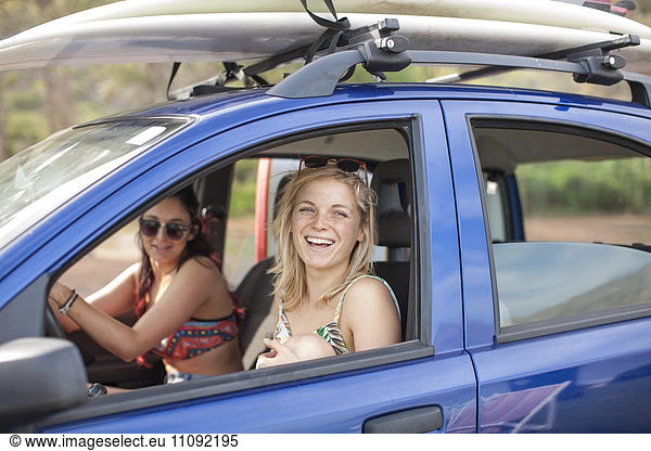 Zwei glückliche junge Frauen im Auto mit Surfbrettern auf dem Dach