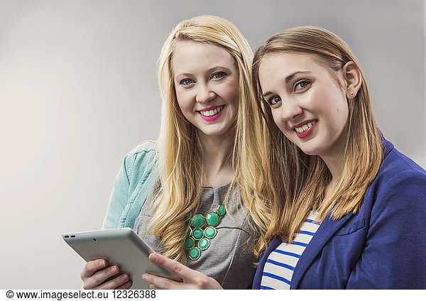 Zwei hübsche junge Frauen  die als Millennial Business Professionals zusammenarbeiten  ein Tablet benutzen und für die Kamera an ihrem Arbeitsplatz posieren; Sherwood Park  Alberta  Kanada