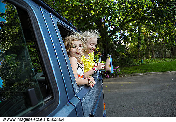 zwei junge Mädchen  die lächeln und sich aus dem Autofenster lehnen