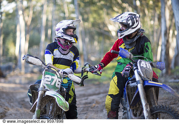 Zwei junge männliche Motocross-Fahrer  die sich auf einer Waldstrecke unterhalten.