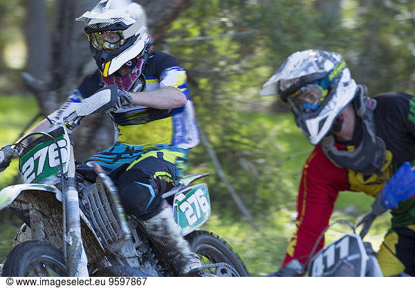 Zwei junge männliche Motocross-Fahrer rasen durch den Wald