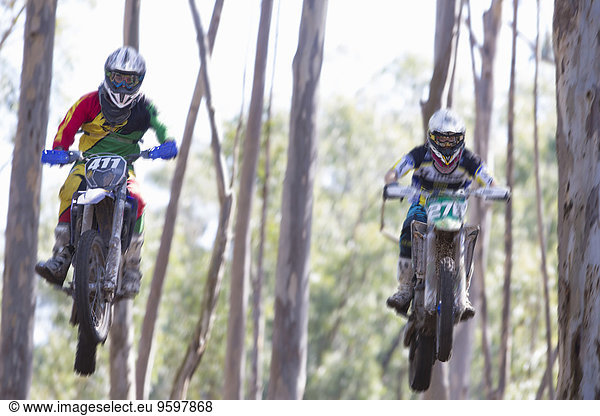 Zwei junge männliche Motocross-Fahrer springen durch den Wald