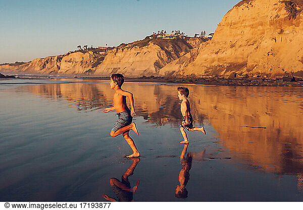 Zwei Jungen laufen bei Ebbe und Sonnenuntergang am Strand entlang.