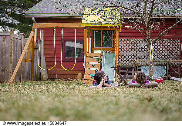 Zwei Kinder lagen im Gras im Hof und unterhielten sich mit einem Spielset im Hintergrund