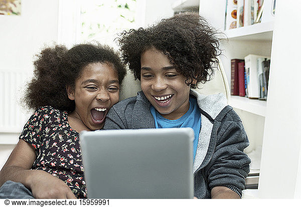 Zwei Kinder sind online und teilen sich lachend einen Laptop.