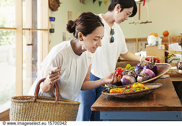 Zwei lächelnde Japanerinnen beim Anblick von frischem Gemüse in einem Hofladen.