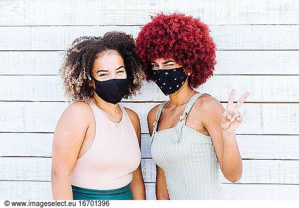 Zwei lateinamerikanische Frauen mit Schutzmaske  die ein Siegessymbol zeigen.