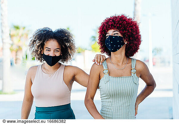 Zwei lateinamerikanische Frauen mit Schutzmaske in unbekümmerter Haltung.