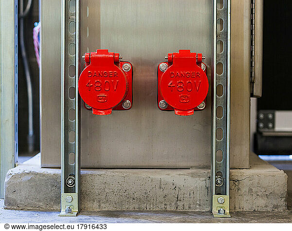 Zwei leuchtend rote Kunststoffabdeckungen  Kappen zur Abdeckung von Stromanschlüssen an einer Wand  Zeichen Danger 480V.