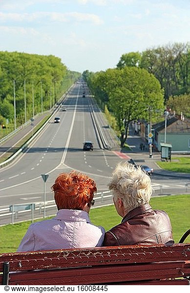 Zwei ältere Frauen unterhalten sich  während sie auf einer Bank sitzen und auf die Autobahn schauen. Alte Freundinnen ruhen sich im Park aus. Rentner verbringen Zeit auf einer Bank im Park sitzend. Gespräch von zwei älteren Frauen.