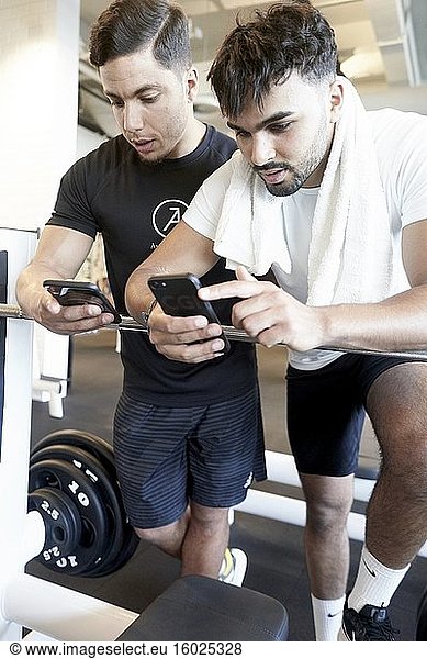 Zwei Männer schauen im Fitnessstudio auf ihre Smartphones