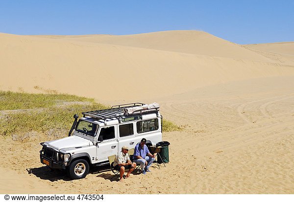 Zwei Männer sitzen vor Geländewagen Landrover Defender in den Dünen des Namib Naukluft Nationalpark  Teil des Namib-Skelettküste Nationalparks  Skeleton Coast  Wüste Namib  Namibia  Afrika