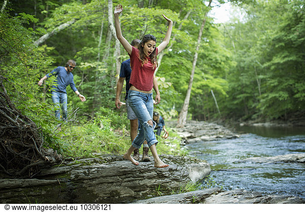 Zwei Männer und zwei Frauen am Flussufer  eine springt über Trittsteine.