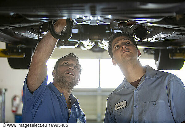 Zwei Mechaniker arbeiten auf einer Hebebühne in einer Reparaturwerkstatt an der Unterseite eines Fahrzeugs